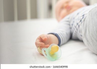 Blurred image of a little baby boy who is peacefully sleeping and holding a pacifier dummy in his hand. Selective focus on a dummy