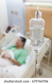 Blurred image of male patient lying on hospital bed, with saline solution bag( IV) as foreground.