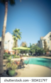 Blurred Image Outdoor Swimming Pool And Woven Rattan Pool Beds With Modern Apartment Houses In Background. Apartment Backyard Landscape With Pool, Palm Trees, Clear Blue Sky, Texas, US. Vintage Filter