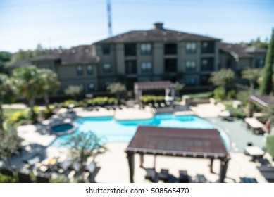 Blurred Image Outdoor Swimming Pool And Woven Rattan Pool Beds With Modern Houses In Background. Elevated View Apartment Backyard Landscape With Swimming Pool, Palm Trees, Clear Blue Sky In Texas, US.