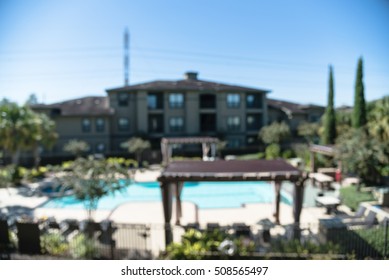 Blurred Image Outdoor Swimming Pool And Woven Rattan Pool Beds With Modern Houses In Background. Elevated View Apartment Backyard Landscape With Swimming Pool, Palm Trees, Clear Blue Sky In Texas, US.