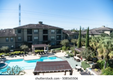 Blurred Image Outdoor Swimming Pool And Woven Rattan Pool Beds With Modern Houses In Background. Elevated View Apartment Backyard Landscape With Swimming Pool, Palm Trees, Clear Blue Sky In Texas, US.