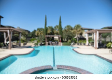 Blurred Image Outdoor Swimming Pool And Woven Rattan Pool Beds With Modern Apartment Houses In Background. Apartment Backyard Landscape With Swimming Pool, Palm Trees And Clear Blue Sky In Texas, US.