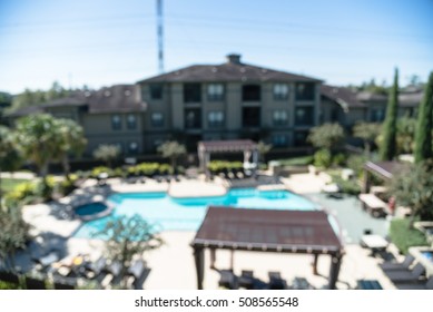 Blurred Image Outdoor Swimming Pool And Woven Rattan Pool Beds With Modern Houses In Background. Elevated View Apartment Backyard Landscape With Swimming Pool, Palm Trees, Clear Blue Sky In Texas, US.