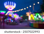 Blurred image of people in funfair amusement park festival in city park at night bokeh background. Summer festival holiday vacation concept.