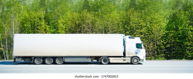 Blurred Image. Red Truck On Road With Blue Blank Container, Cloudy Sky, Cargo Transportation Concept. Side View.