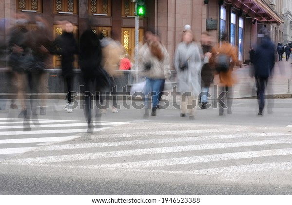 Blurred image of the road with people on a sunny\
day. People walking on the street on a pedestrian crossing, a crowd\
of people on shopping\
street.