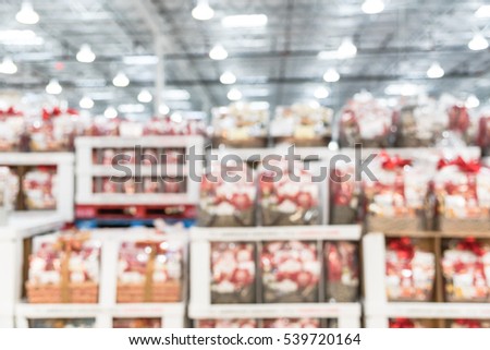 Blurred image row of Christmas hamper baskets in wholesale store. Variety Holiday gift baskets with chocolate Santa, cookies, wine, tea sale. Defocused background interior warehouse, business concept.