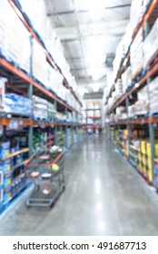 Blurred image shelves in modern distribution warehouse with shopping cart. Defocused background of industrial warehouse interior aisle, inventory, hypermarket, wholesale, logistic and export concept.