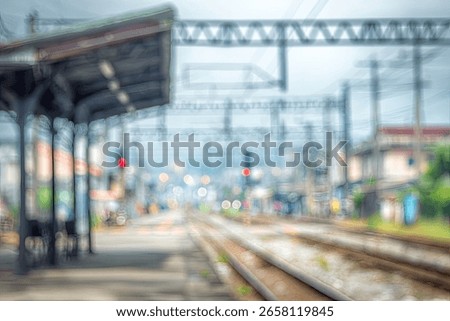 A blurred image of a train station platform with railway tracks extending into the distance.