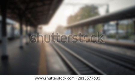 A blurred image of a train station platform with railway tracks stretching into the distance, bathed in soft sunlight.