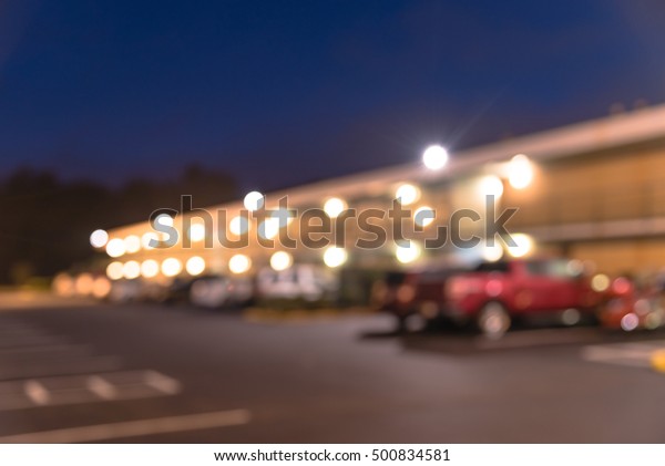 Blurred image of two story motel with parking lot\
in foreground at blue hour in Hope, Arkansas, US. Generic budget\
motel in suburban roadside location with row of parked cars next to\
the rooms.
