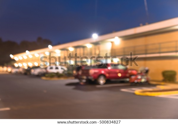 Blurred image of two story motel with parking lot\
in foreground at blue hour in Hope, Arkansas, US. Generic budget\
motel in suburban roadside location with row of parked cars next to\
the rooms.