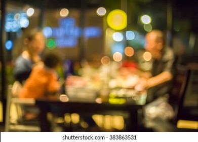 Blurred Image Of Typical Chinese Family Gathered Around  Table In Restaurant At Night