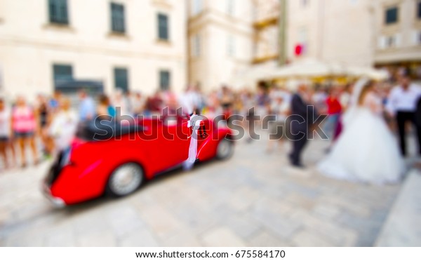 Blurred\
image. Wedding at the church with the classic red car in town.\
wedding couple outside the church with red\
car.