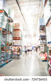Blurred image wholesale store with big boxes of product from floor to ceiling. Large warehouse in USA. Defocused industrial distribution storehouse abstract background. Customer shopping with carts.