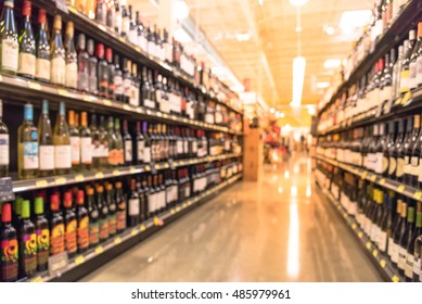 Blurred image of wine shelves display in supermarket. Defocused  Rows of Wine Liquor bottles on the store shelf. Alcoholic beverage abstract background. Alcohol drink market concept.