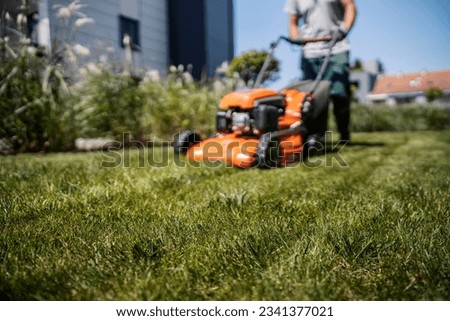 Blurred image of a worker maintaining the grass with a lawn mower.