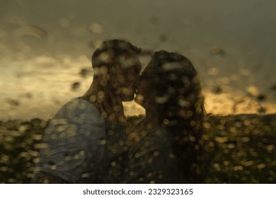 blurred image of a young couple guy and girl kissing on the lips at sunset in the rain, shot through glass with raindrops. High quality photo - Powered by Shutterstock