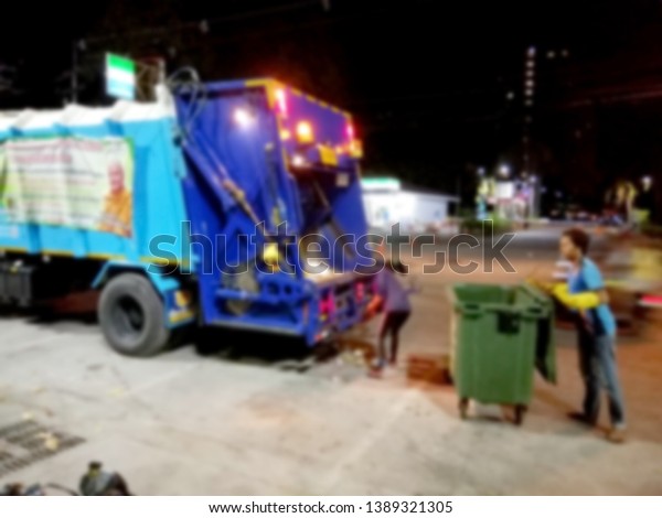 Blurred images\
of municipal garbage collectors are picking up garbage in the\
garbage truck at night without\
anyone.