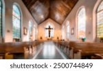 Blurred interior of a small, intimate church with wooden pews, large stained glass windows, and a prominent crucifix at the altar, creating a peaceful and reflective atmosphere.