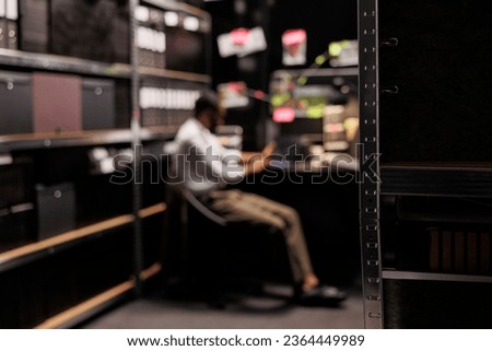 Blurred investigator solving crime, sitting at workplace table in office. Policeman working overtime at desk, conducting investigation and analyzing evidence at night time