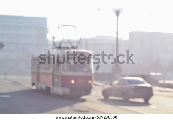 The blurred landscape of city streets\
with moving cars and tram during a foggy morning. Artistic\
reception of a blurred landscape photo with a bokeh\
effect