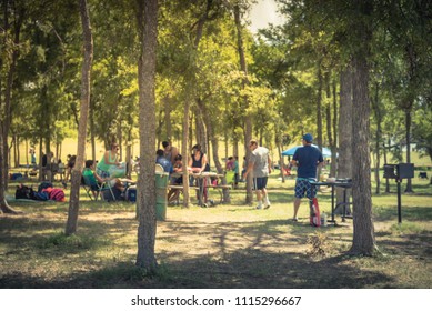 Blurred Large Group Of Friend, Family Members Enjoy Barbecue On Lakeside Area. Outdoor Camping At Natural Park With Picnic Table In Grand Prairie, Texas, USA. Outside Party And BBQ Concept