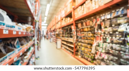Blurred a large hardware store, tools and material. Defocused interior of home improvement retailer, racks of door hardware, weather proofing and lockset floor to ceiling. Customers shopping. Panorama