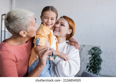 blurred lesbian woman holding key from new apartment near girlfriend and adopted daughter