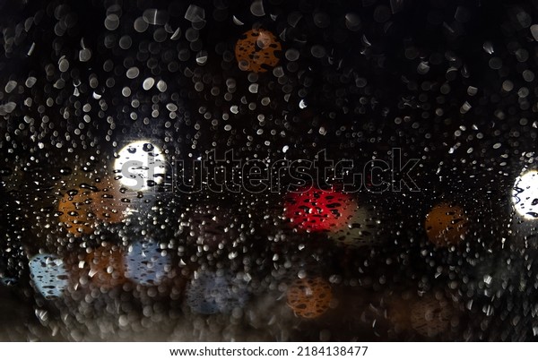Blurred lights behind car\
window with water droplets. Raindrops on the windshield of the car\
at night.