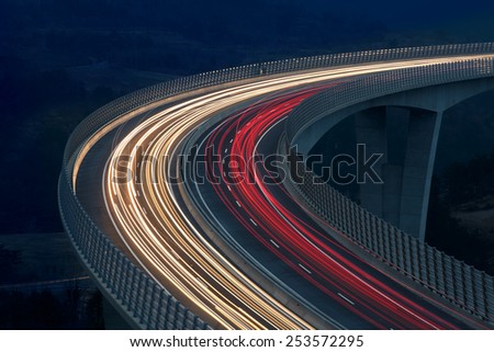 Blurred lights of vehicles driving on a tall viaduct with wind barriers, long exposure