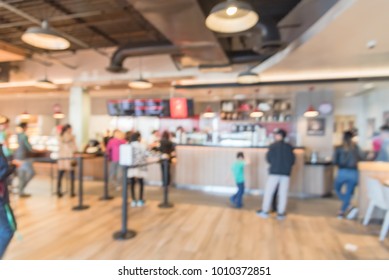 Blurred Long People Queuing Behind Stanchion Barriers At Check-out Counter At Bakery In Texas, USA. Large Wall Mount Led Menu Board Digital Signage. Abstract Background Diverse Multiethnic Crowd Wait