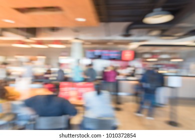 Blurred Long People Sit And Stand Queuing Behind Stanchion Barriers Check-out Counter At Bakery In Texas, USA. Large Wall Mount Led Menu Board Digital Signage. Abstract Diverse Multiethnic Crowd Wait