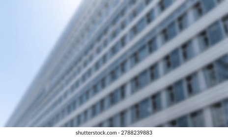 A blurred low angle perspective of a modern glass office building facade featuring repetitive window patterns against a bright sky
