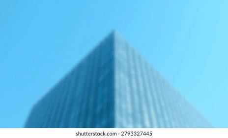A blurred low angle view of a modern glass skyscraper corner against a clear blue sky background showing architectural lines and geometric shapes.