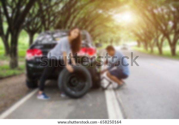  blurred man helps a woman to replace the wheel on\
the car