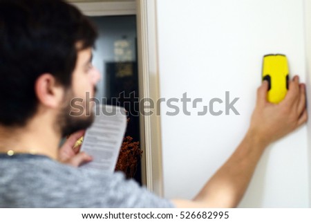 Blurred man using stud finder to search apartment wall for studs and live wires