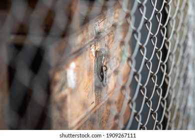 (Blurred) Metal Pin Locking System Of The Item Wooden Box Which Is Contain Working Equipment In The Storage Room, Barricade By Wire Mesh Fence (foreground). Close-up And Selective Focus Object Photo. 