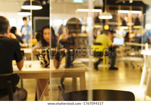 Blurred modern restaurant or cafeteria\'s\
interior with clear plastic barriers / dividers on table as part of\
safety protection for customers. New normal & Social\
distancing during Covid-19 pandemic\
