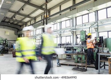 Blurred Motion Of Business People Walking With Manual Worker In Background At Industry