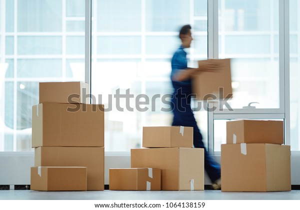 Blurred motion of\
contemporary worker with packed box walking to new office while\
delivering it to client