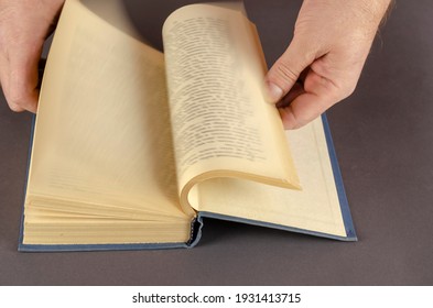 Blurred Motion Of Hand Turning Page Over gray Background. Male hands quickly leaf through an old book with yellowed pages. Middle-aged man, Caucasian.