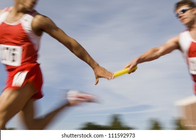 Blurred motion male runners passing baton in relay race