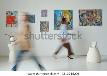 Blurred motion of people passing through the paintings on the wall in art gallery