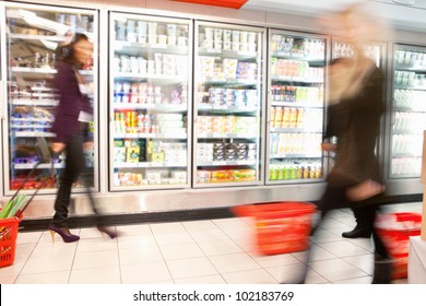 Blurred Motion Of People Walking Near Refrigerator In Shopping Centre With Baskets