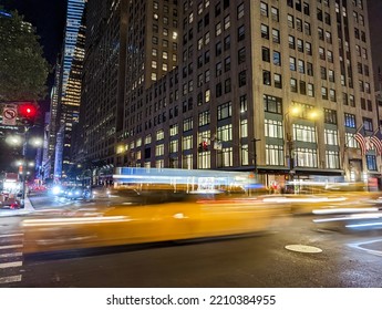 Blurred motion of a yellow taxis driving down the street through New York City at night with the building lights in the background - Powered by Shutterstock
