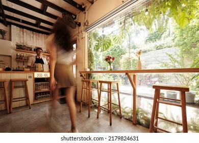 Blurred motion of young woman walking to coffeeshop counter to order morning coffee