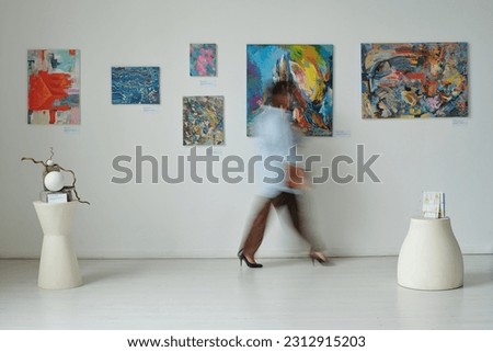 Blurred motion of young woman walking through paintings on the wall in art gallery