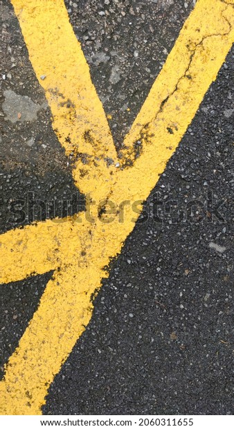 Blurred no parking area sign on asphaltic\
surface, Yellow crossing sign on the textured floor, Yellow logo on\
grey color background